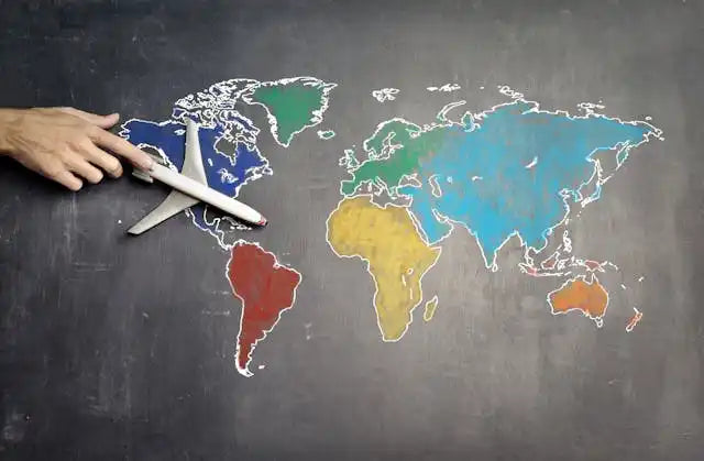 Hand holding a toy airplane over a chalk-drawn world map with colorful continents.