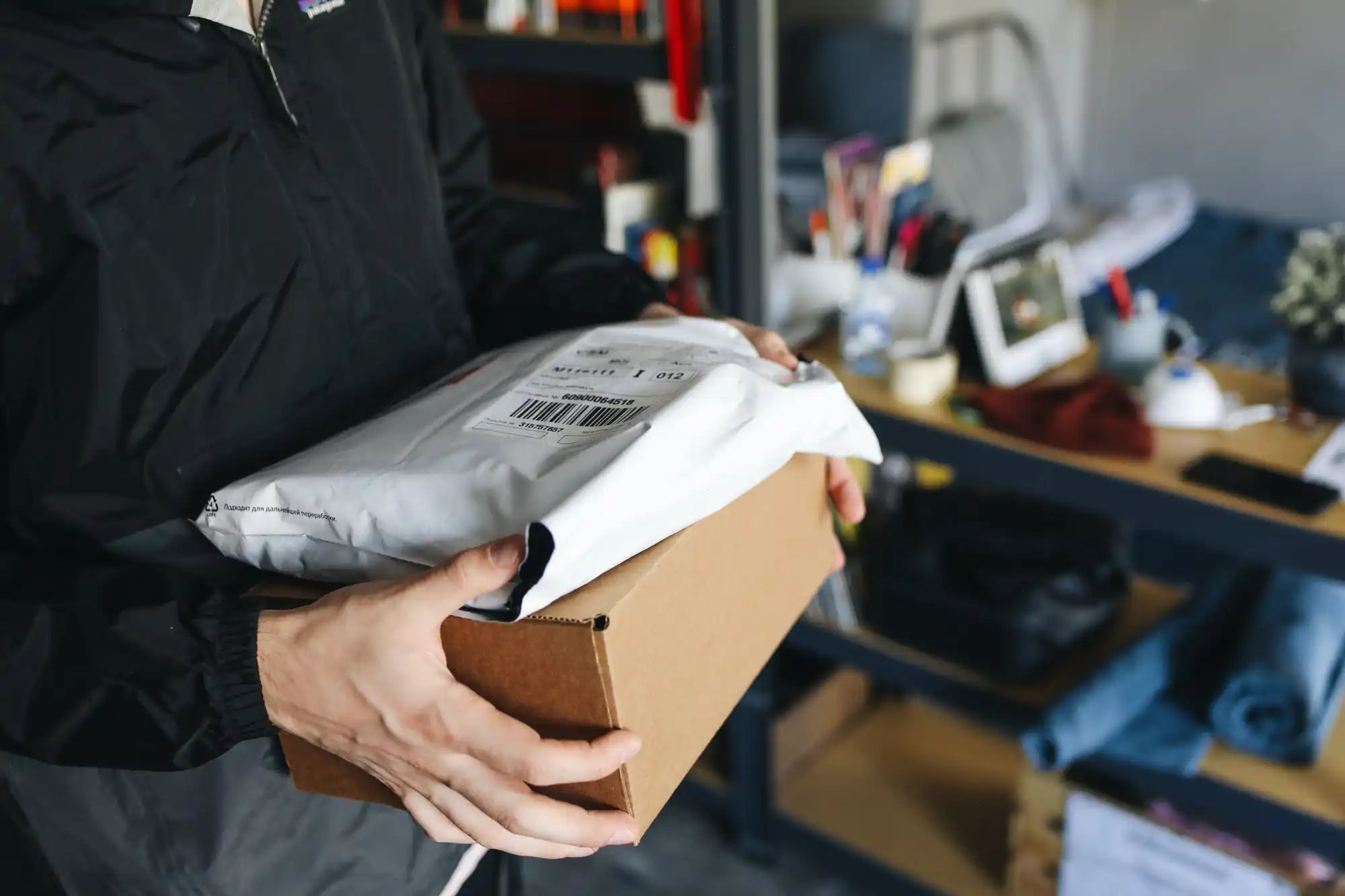Hands holding a cardboard box with a white package on top.