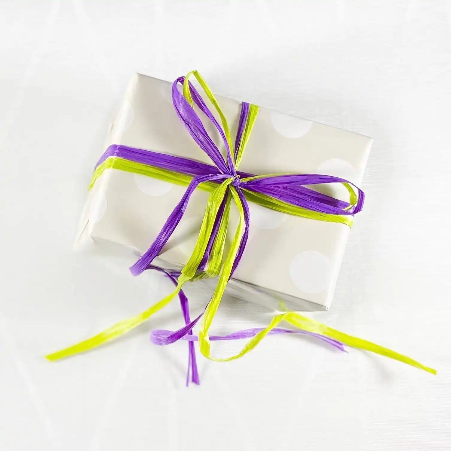 White gift box wrapped with purple and lime green ribbons tied in a bow.